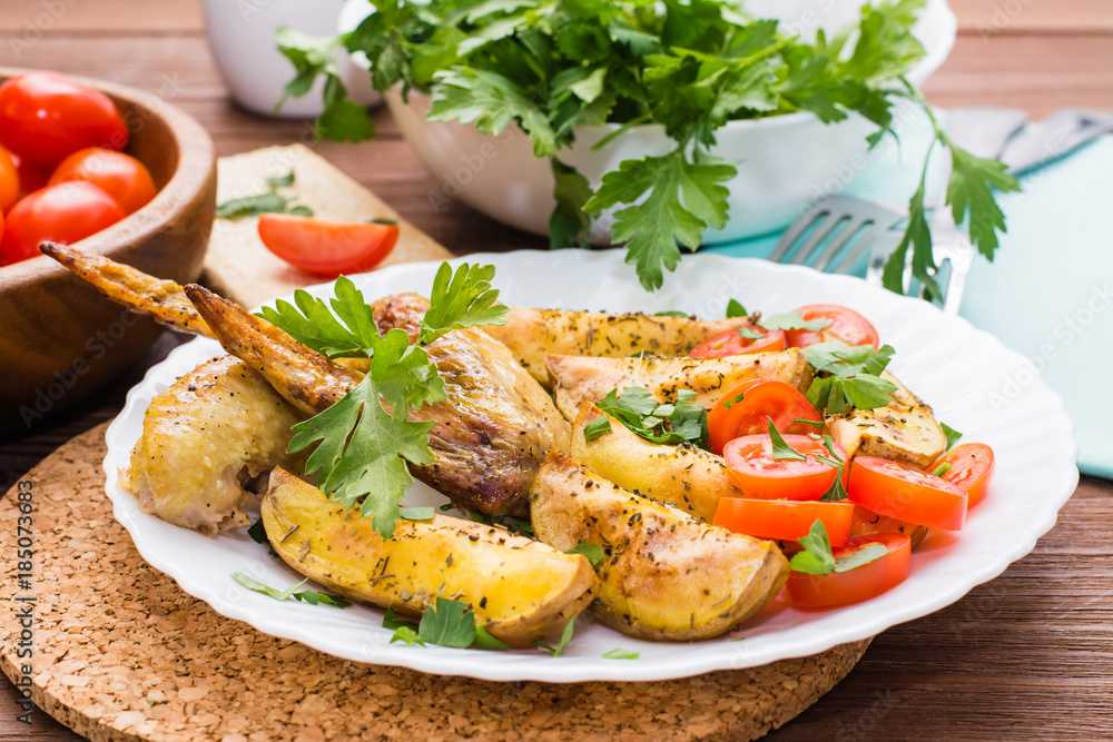 Baked chicken wings and potatoes, fresh tomatoes and greens on a plate