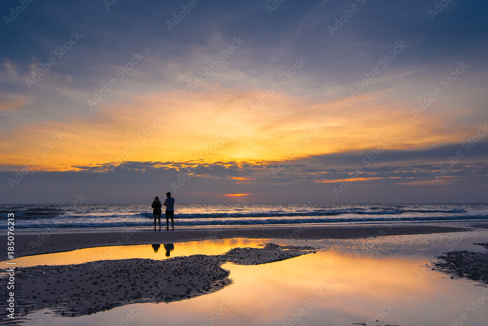 Romantic scene of a couple silhouette of a couple enjoying on the beach watching the sunrise in the morning.