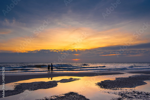 Romantic scene of a couple silhouette of a couple enjoying on the beach watching the sunrise in the morning.