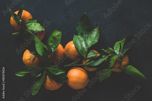Tangerines with green leaves on dark background. Top view, toned image, moody still life