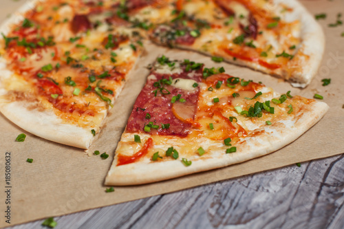 Pizza with a thin crust with cheese, bacon, pepper and herbs on a light wooden background
