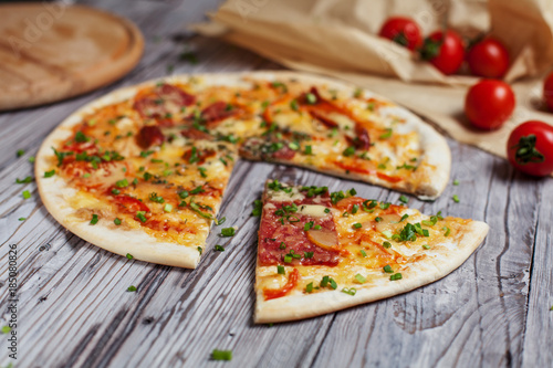 Pizza with a thin crust with cheese, bacon, pepper and herbs on a light wooden background