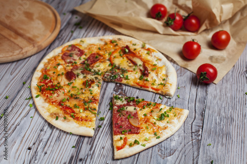 Pizza with a thin crust with cheese, bacon, pepper and herbs on a light wooden background photo