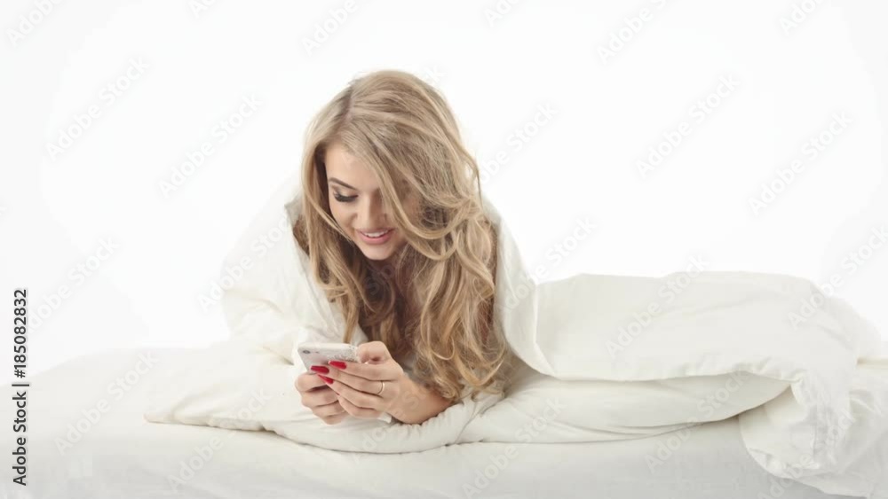Smiling sexy woman looking at mobile phone lying down on the bed Smiling sexy woman looking at mobile phone lying down on the bed