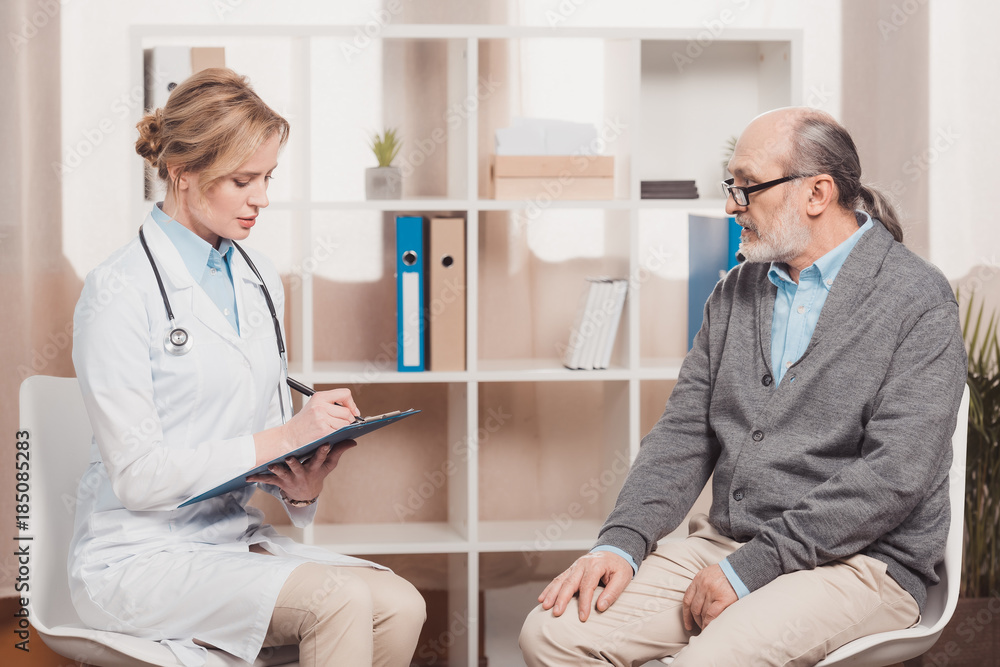 Fototapeta premium doctor in white coat with notepad listening to patients complaint in clinic