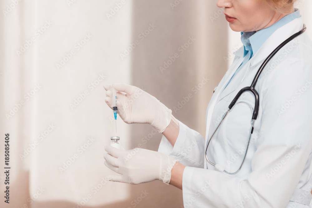 partial view of doctor in white coat and medical gloves holding syringe for injection in hands in clinic partial view of doctor in white coat and medical gloves holding syringe for injection in hands in clinic