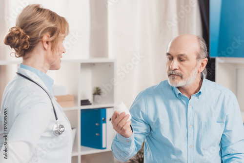 portrait of senior patient looking at medicines in hand with doctor near by in clinic