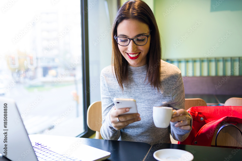 Beautiful young woman using mobile phone while drinking coffee in the cafe. Beautiful young woman using mobile phone while drinking coffee in the cafe.