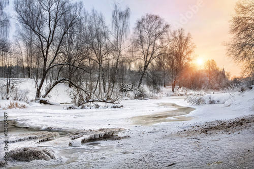 Замерзшая река в заснеженном лесу и закатное солнце Frozen river in the snowy forest and the setting sun