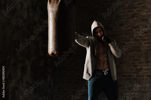 An African American guy trains in a vintage gym and fists his boxing bag fists. Concept of: gym, fitness, boxing, success, workout and power © Kitreel