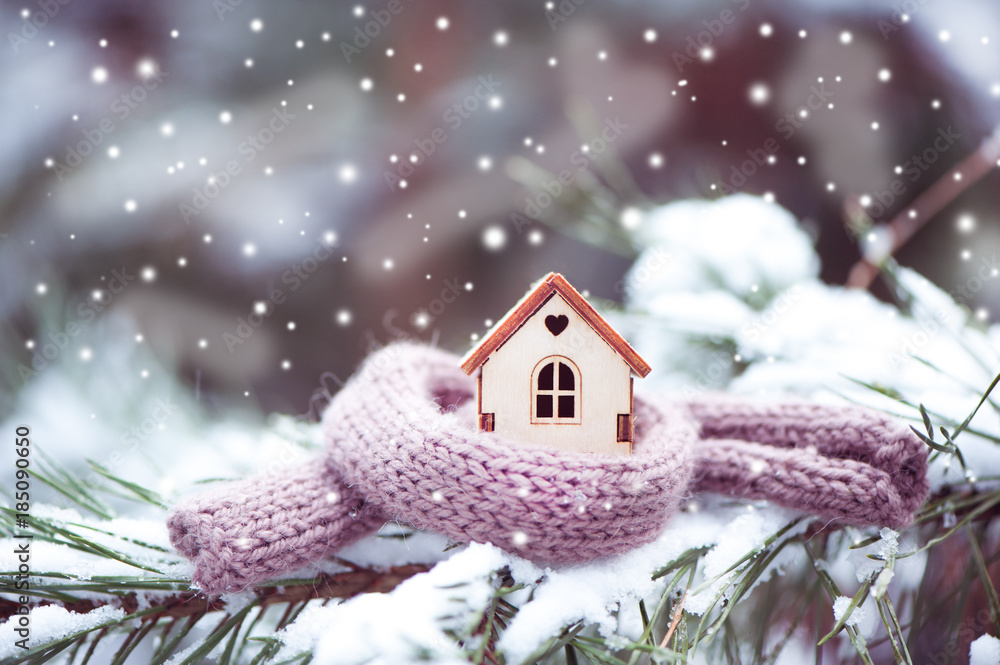 Christmas Toy house is wrapped in a warm scarf, it's snowing.on a natural natural background of a real fir in the snow, toned. Concept of winter, Christmas, new year, - obrazy, fototapety, plakaty 