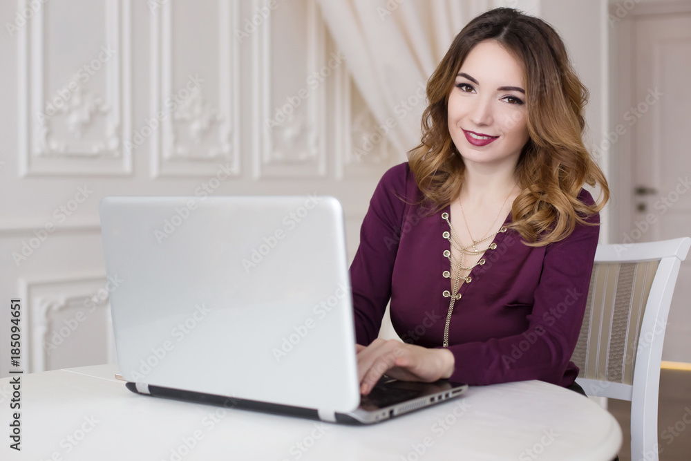 Beautiful woman is sitting in an expensive kitchen behind a laptop. Work at home, realtor, online store. Beautiful woman is sitting in an expensive kitchen behind a laptop. Work at home, realtor, online store.