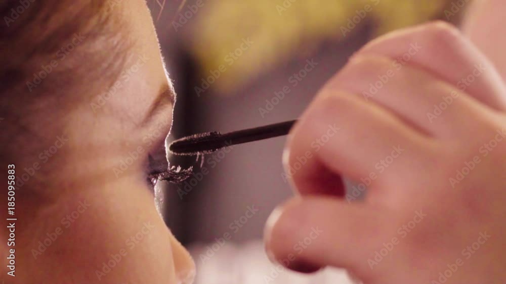 Slow motion. Extreme close up of the female eyes. Professional makeup artist applying mascara on the eyelashes of the model. Rear view Slow motion. Extreme close up of the female eyes. Professional makeup artist applying mascara on the eyelashes of the model. Rear view