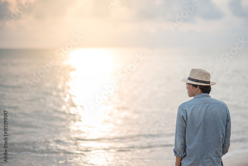 Young Asian man with jean shirt and hat standing on the beach and looking beautiful sunset, vacation time and summer holiday concepts © zephyr_p