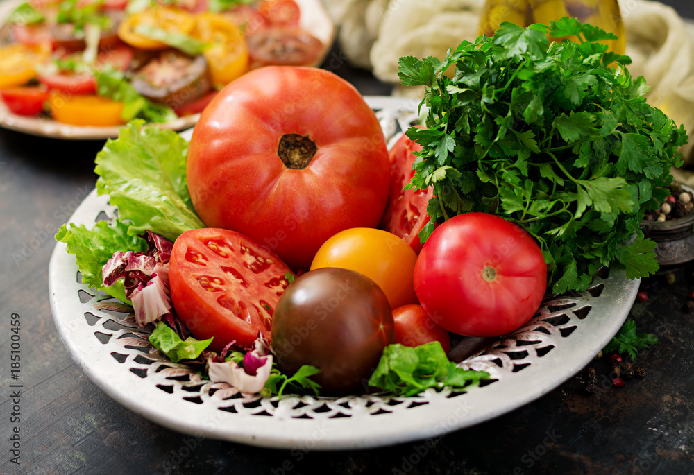 Tomatoes of different colors with green herbs in a bowl on a black background Tomatoes of different colors with green herbs in a bowl on a black background