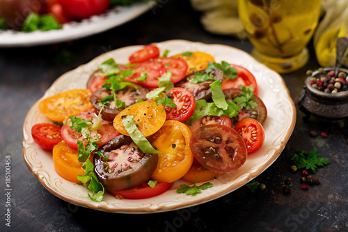 Summer salad of tomatoes of different colors with green herbs and pepper.
