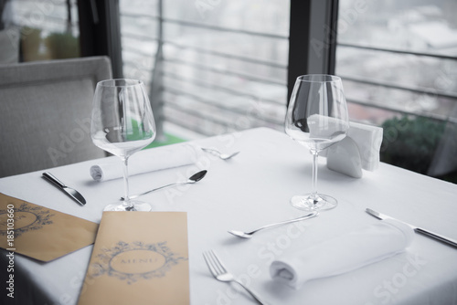 close up view of arranged cutlery, empty wineglasses and menu on table with white tablecloth in restaurant