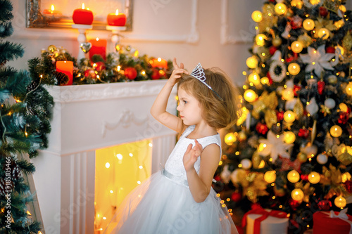 Little girl posing in a dress near the mirror whike adjusting crown on her head. photo