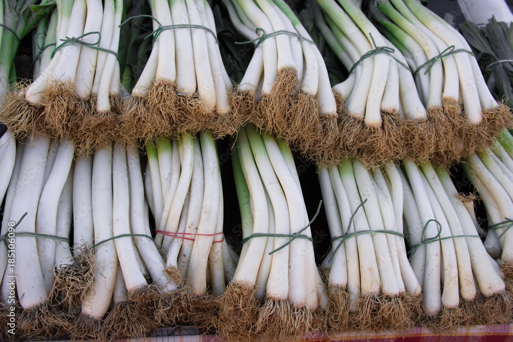 Fototapeta premium Porri freschi esposti su una bancarella di mercato all’aperto. Colori naturali, disposizione ordinata, luce diurna. Scena ideale per temi legati ad agricoltura, alimentazione e filiera corta.