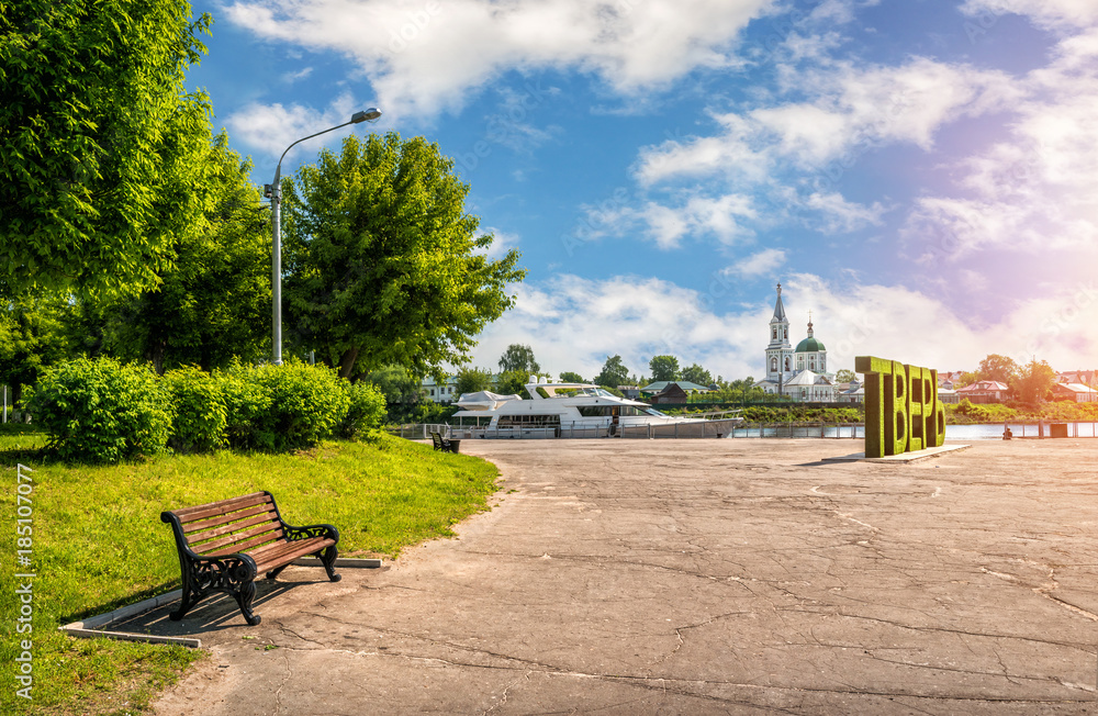 Скамейка у причала реки в Твери и белая яхта и храм монастыря Bench at the pier of a river in Tver and a white yacht and the temple of the monastery