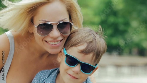 Young happy smiling mother in sunglasses hugging her son in the park photo