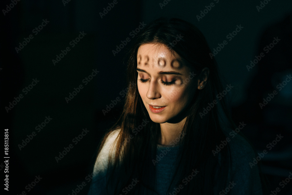 Low key portrait of young mysterious woman with close eyes and shadow of numerals twenty two o'clock on her forehead. Time run away concept. Low key portrait of young mysterious woman with close eyes and shadow of numerals twenty two o'clock on her forehead. Time run away concept.