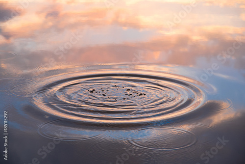 Water drop falling on water surface in evening  sunlight with reflection