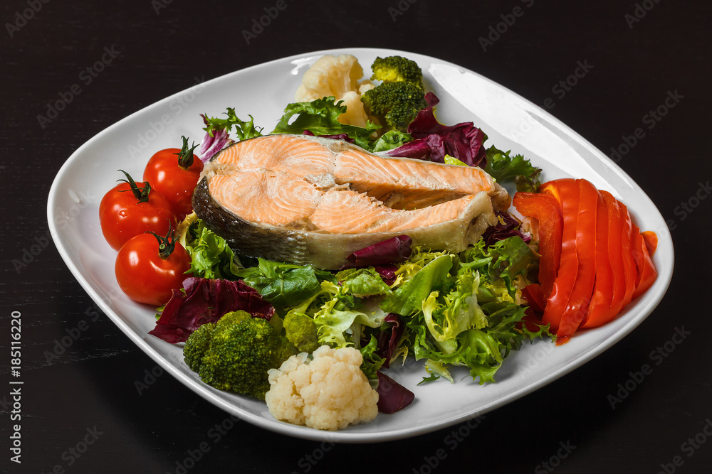 Salmon steak on a bed of mixed salad with fresh pepper and cherry tomatoes, steamed cauliflower and broccoli on a white square plate Salmon steak on a bed of mixed salad with fresh pepper and cherry tomatoes, steamed cauliflower and broccoli on a white square plate