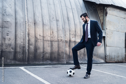 smiling businessman in suit playing soccer on street photo