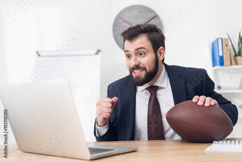 portrait of businessman with rugby ball at workplace with laptop in office