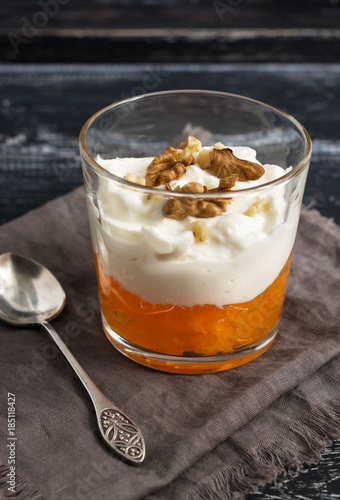 Yoghurt with persimmon and nuts in a glass. Dessert on a wooden table with a spoon and napkin
