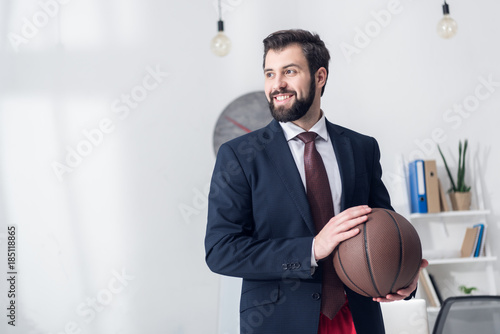 Fototapeta Naklejka Na Ścianę i Meble -  portrait of businessman in jacket holding basketball ball in office