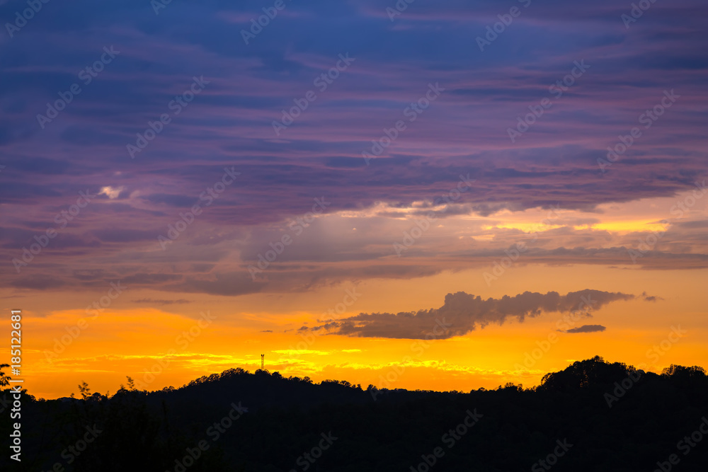 The silhouette of the landscape during the sunset on a summer evening, a bright orange light makes its way between the thick blue clouds. Cloudscape in Adler, Sochi, Russia.