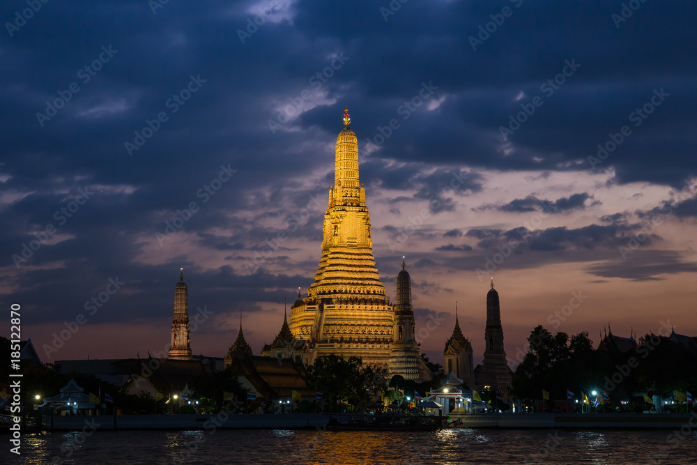 Pagoda at temple of dawn or Wat Arun in Bangkok, Thailand when sunset at twilight with scattered cloud and blue sky in the background and Chao Phraya river in the foreground.  