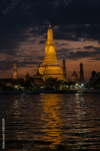 Pagoda at temple of dawn or Wat Arun in Bangkok  Thailand when sunset at twilight with scattered cloud and blue sky in the background and Chao Phraya river in the foreground.  