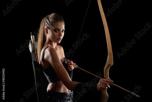 Billede på lærred Studio portrait of a gorgeous young long haired female warrior looking to the camera holding a bow posing on black background copyspace archer archery medieval character Amazon tribe