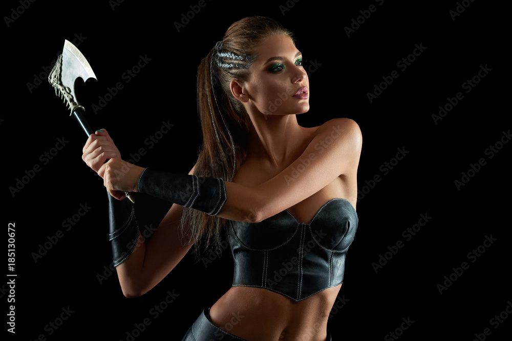 Horizontal shot of a stunning female fighter in leather traditional Amazons tribe battledress posing fiercely with an axe on black background historical culture warrior protector sexy. Horizontal shot of a stunning female fighter in leather traditional Amazons tribe battledress posing fiercely with an axe on black background historical culture warrior protector sexy.
