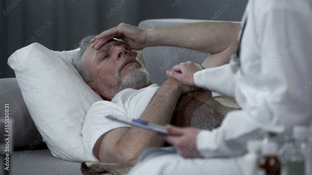 Fototapeta premium Retired man lying in bed and complaining doctor about headache, high temperature