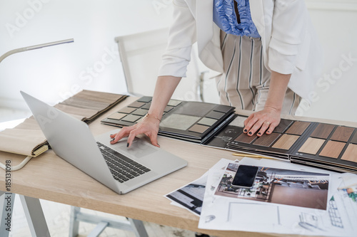 Hands of unrecognisable woman interior designer working with material palette and typing on her laptop.