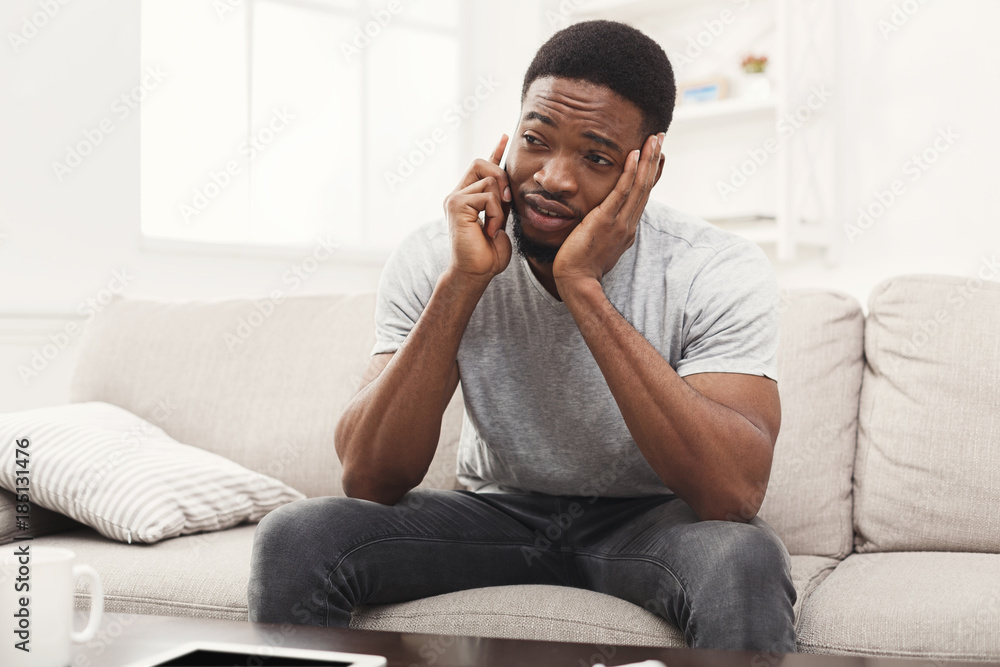 Sad young man talking on mobile at home Sad young man talking on mobile at home