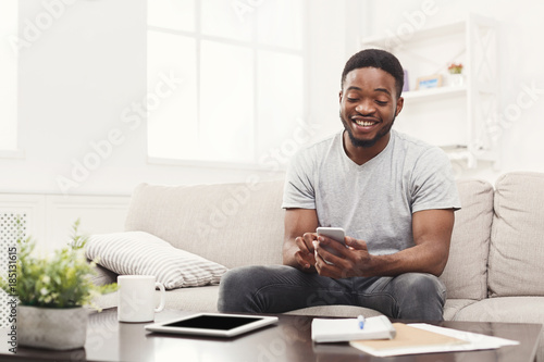 Happy young man at home messaging on mobile