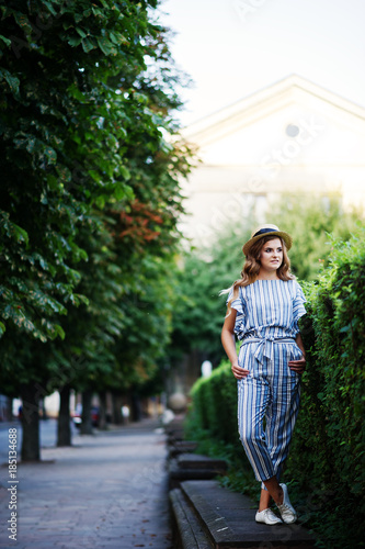 Portrait of a fabulous young woman in striped overall walking on the barrier in the park.