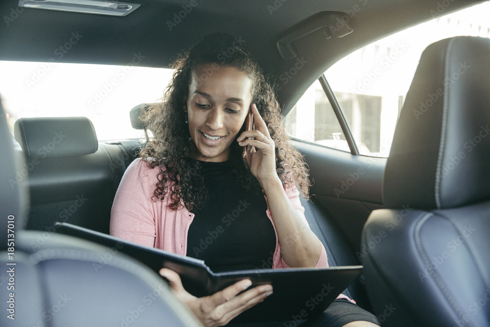Businesswoman looking at file while talking on smart phone in car Businesswoman looking at file while talking on smart phone in car