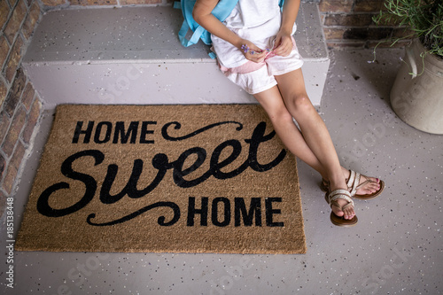 High angle view of girl sitting on retaining wall by doormat