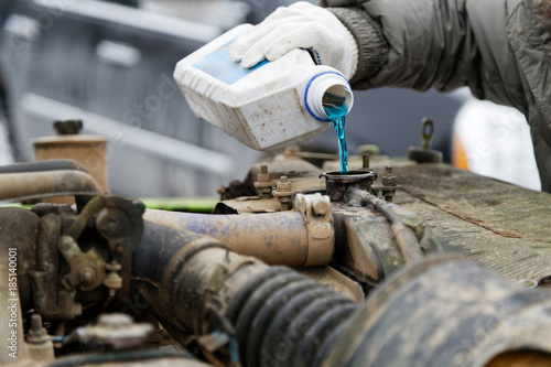 An auto mechanic pours antifreeze into the radiator of an old car engine. Shallow focus. photo