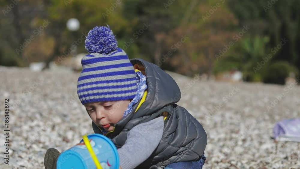 A small child smiles into the camera and plays on the beach with toys. A small child smiles into the camera and plays on the beach with toys.