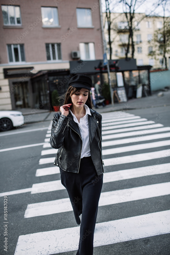 Beautiful girl with sunglasses. A model in a stylish wide-brimmed hat at a pedestrian crossing. Harmoniously similar clothes in gray tones. Street style shooting. Women's fashion.