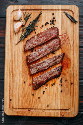 Φωτογραφία Sliced well-done grilled steak on wooden cutting board with rosemary and spices, close up