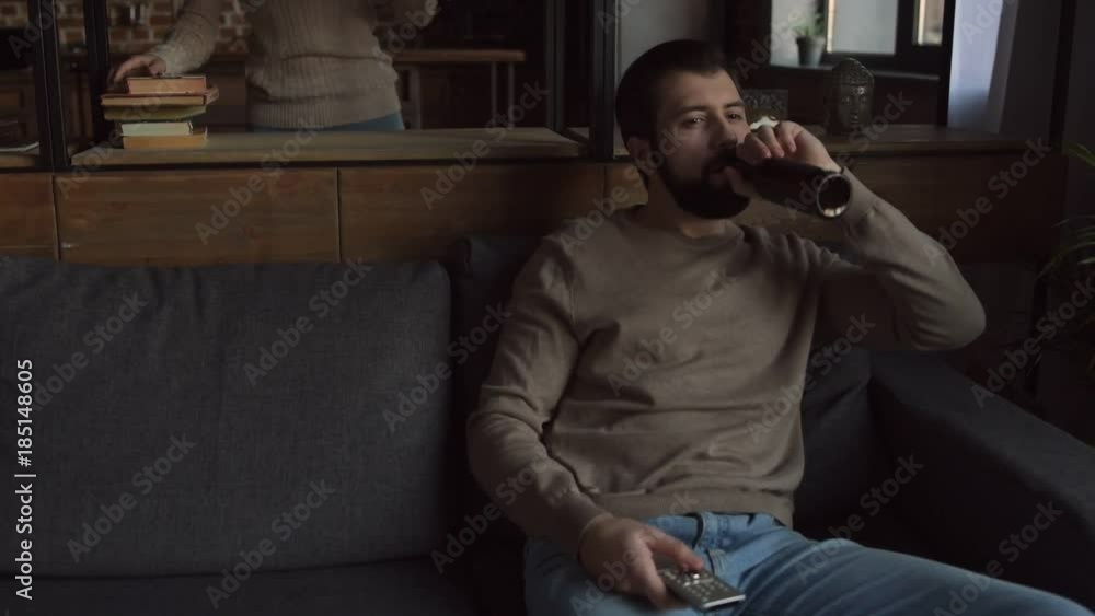 Indifference. Young selfish man sitting on the sofa while drinking beer and paying no attention to his girlfriend Indifference. Young selfish man sitting on the sofa while drinking beer and paying no attention to his girlfriend