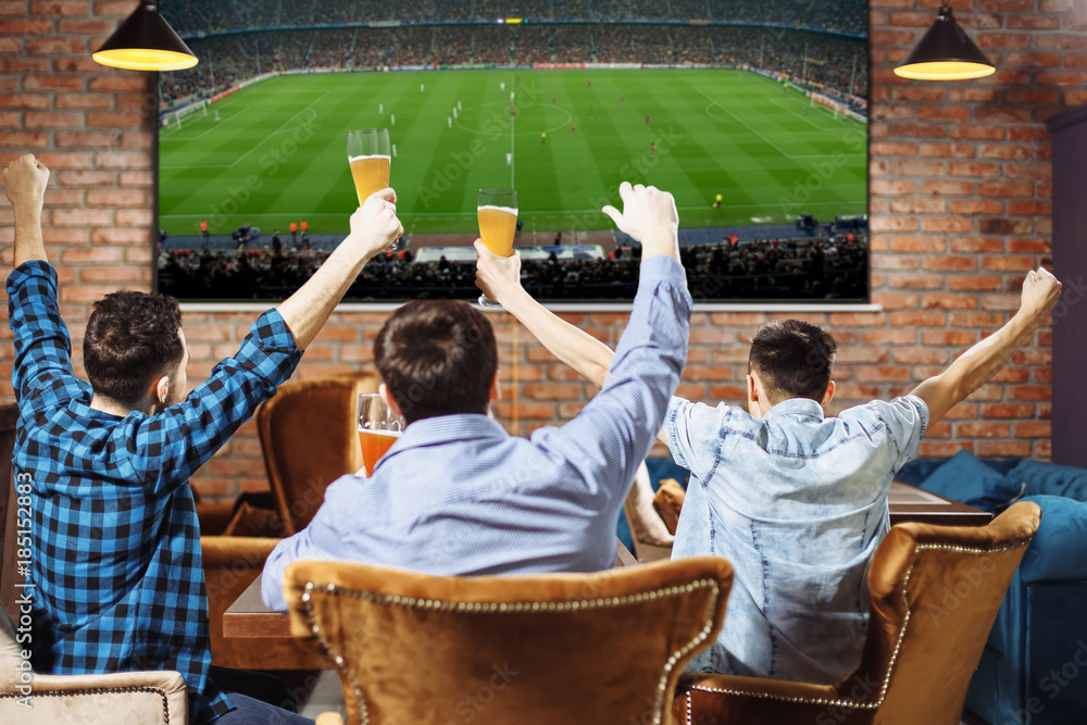 Group of young men cheering on their favorite football team watching the game on TV at the local